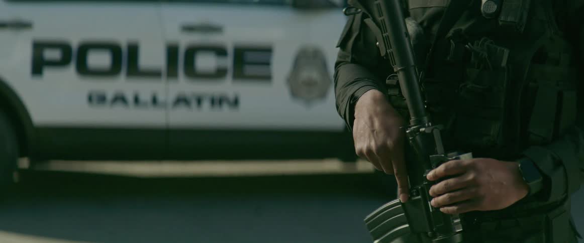 Police officer holding a gun in front of a vehicle