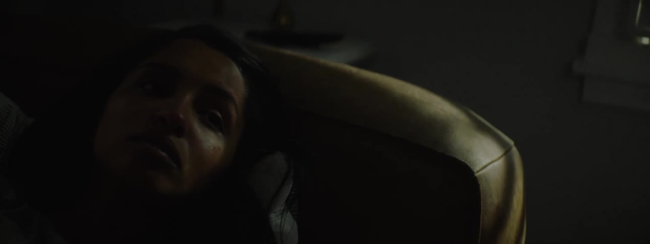 Young woman lying on a couch beside a window in a dark room with the warm glow of the setting sun streaming through the window and reflecting into the room