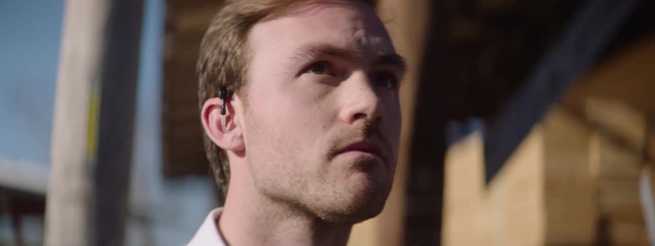 A man with an earpiece looks focused and alert in the bright daylight