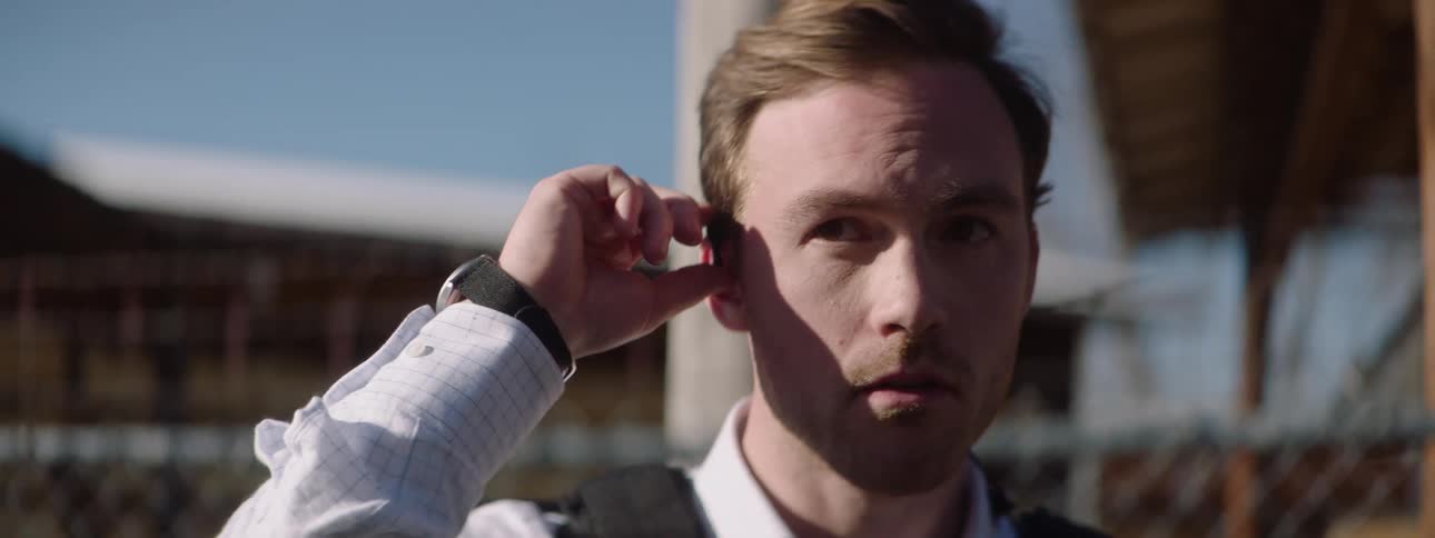 In the video a man with a backpack and an earpiece is seen walking he is wearing a white collared shirt and looks over his shoulder as if he is being followed