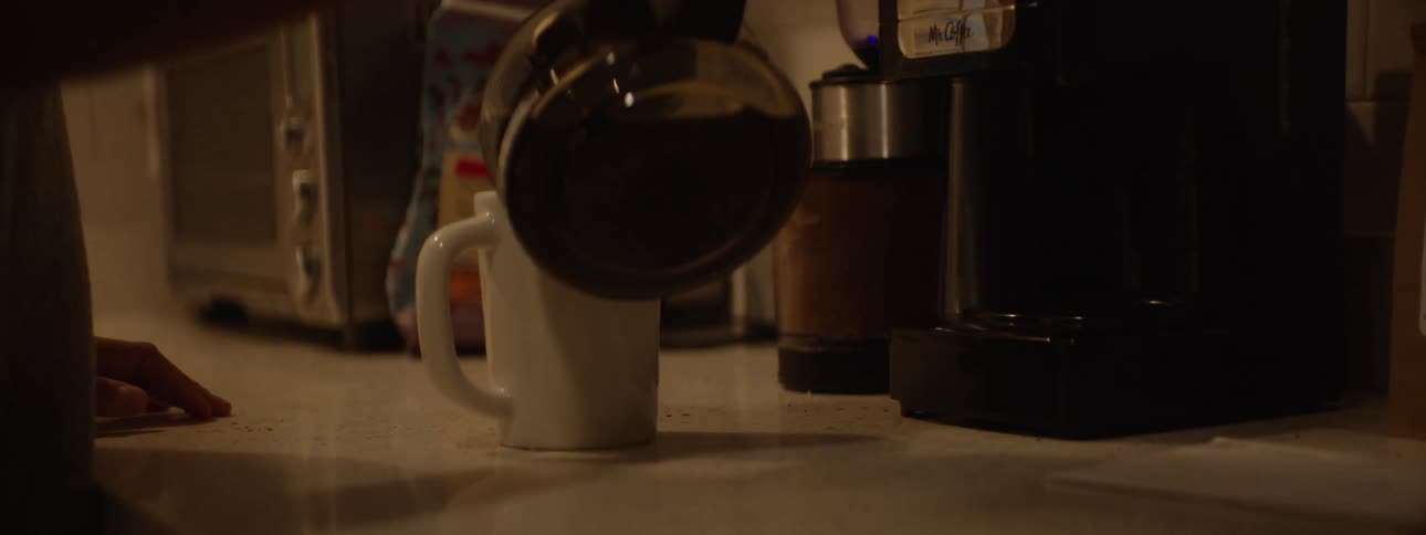 A woman grabs a mug from the cabinet and pours herself a cup of coffee