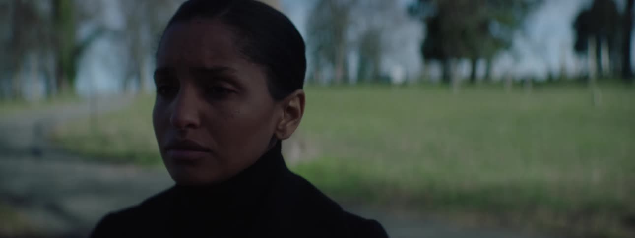 With a somber expression a woman dressed in black turns and walks away through a cemetery