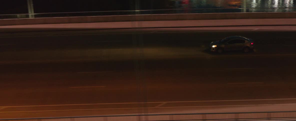 A lone car driving on a highway at night with streetlights casting a warm glow that illuminates the road ahead