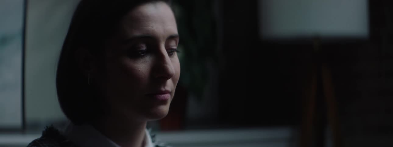Woman with a serious expression looks down in a dimly lit setting