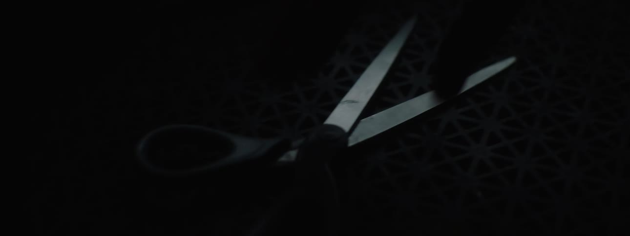 A hand picks up a pair of scissors lying on a black surface