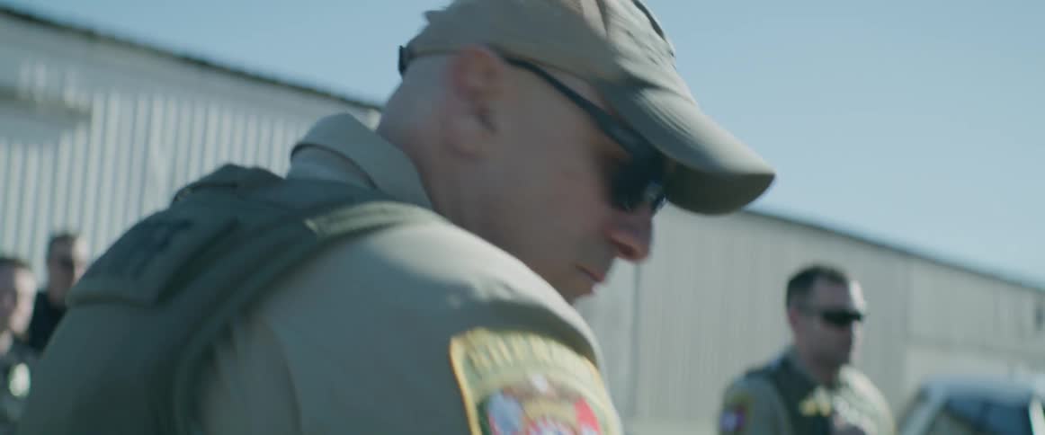 Police officers standing in front of police vehicles and a camera that changes position to show another police officer holding a roll of tape