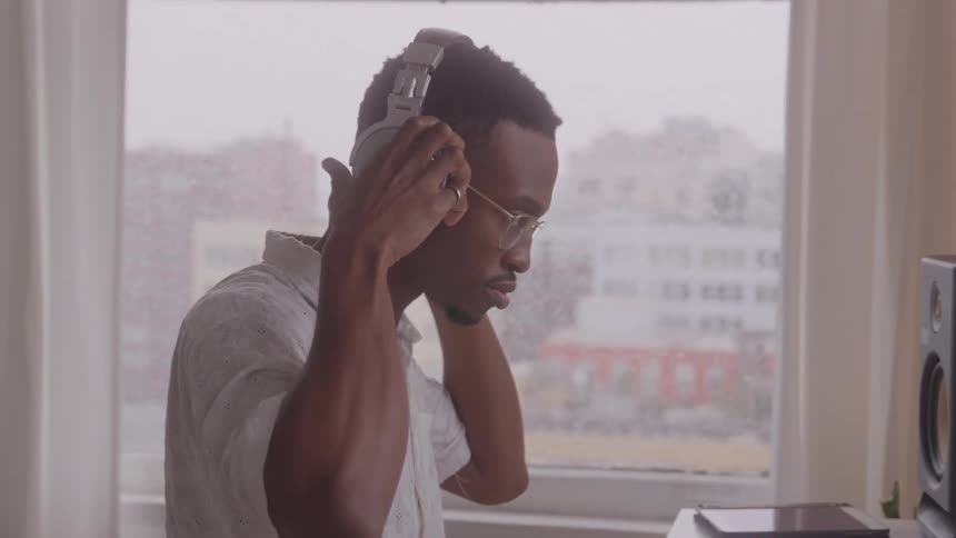 Man puts on headphones while working on a computer near the window