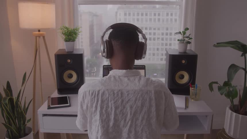 A person sits at a desk looks at a computer screen and works while wearing headphones