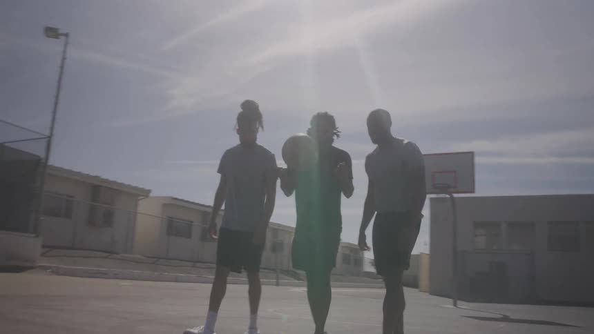 Three friends walking on a basketball court with a ball in hand