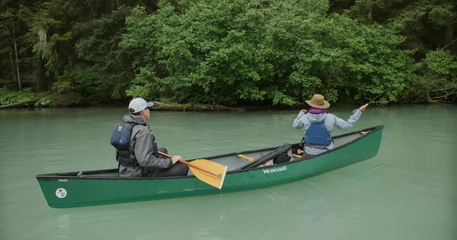 Two people paddling in a green canoe on a river surrounded by trees