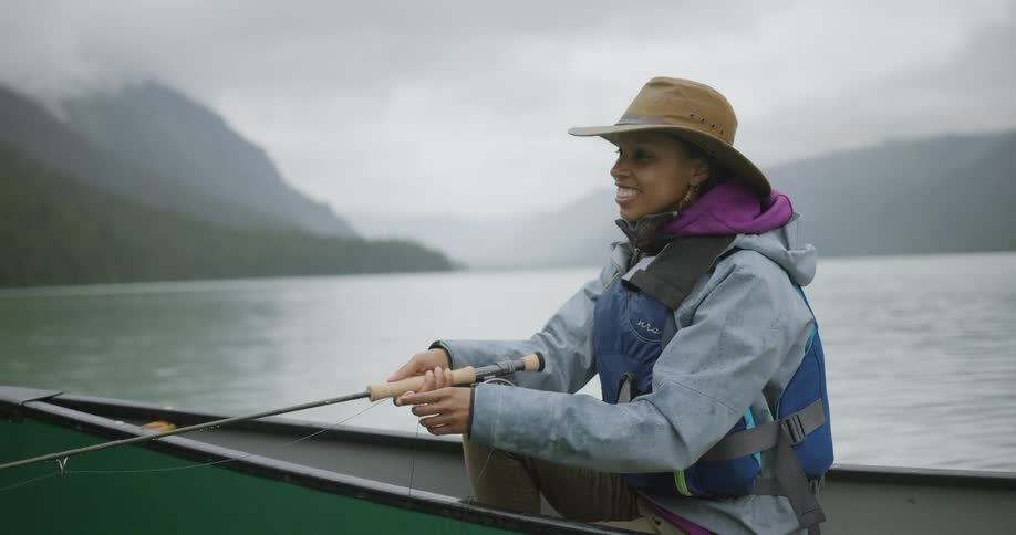 Woman smiles while holding a fishing rod sitting in a canoe on the lake
