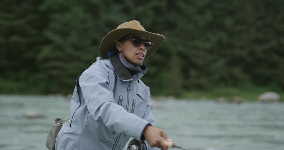 Woman wearing a hat and sunglasses fishing with a rod in a river