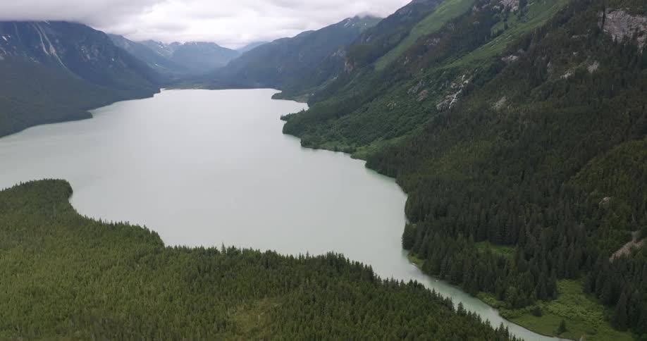Aerial view of a lake surrounded by dense forests and cloudcovered mountains