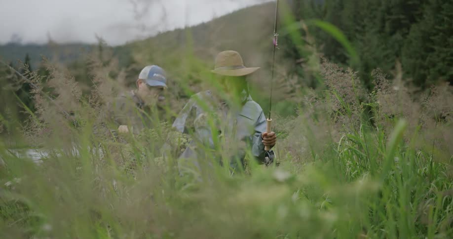 Two fishermen walking through tall grass near the forest