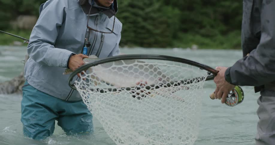 Two people in a river with one of them holding a freshly caught fish