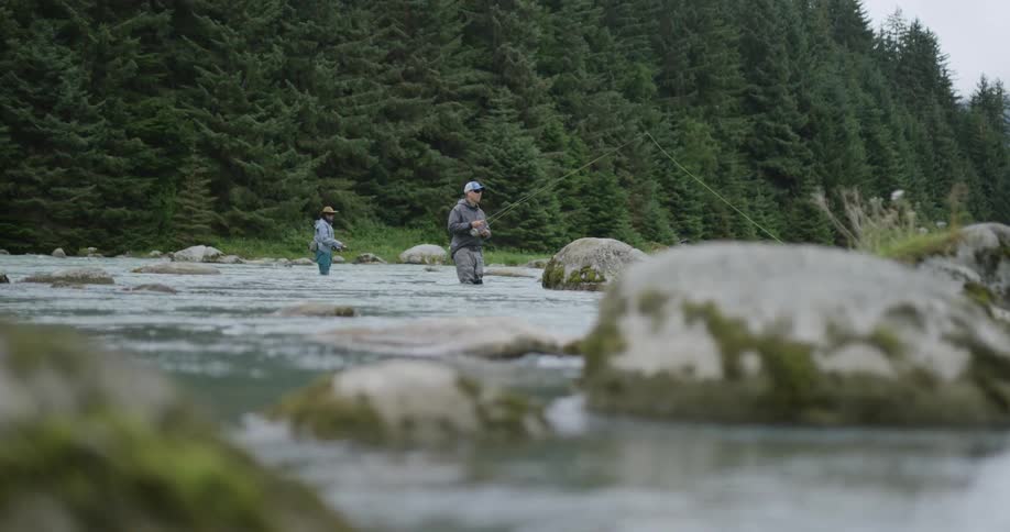 Two men wading in a river use fishing rods to try to catch fish