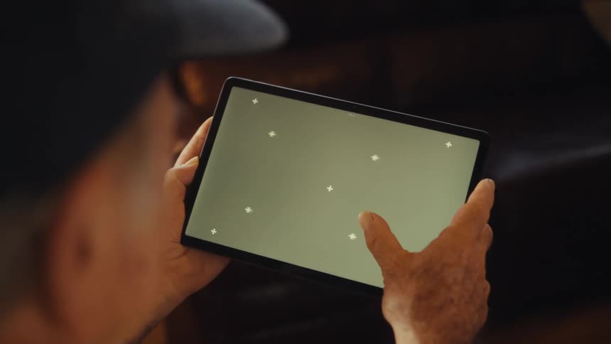 Elderly man sitting while holding a tablet in landscape orientation interacting with the screen