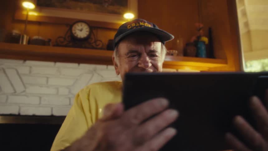 Elderly man in a wheelchair is smiling and interacting with a tablet