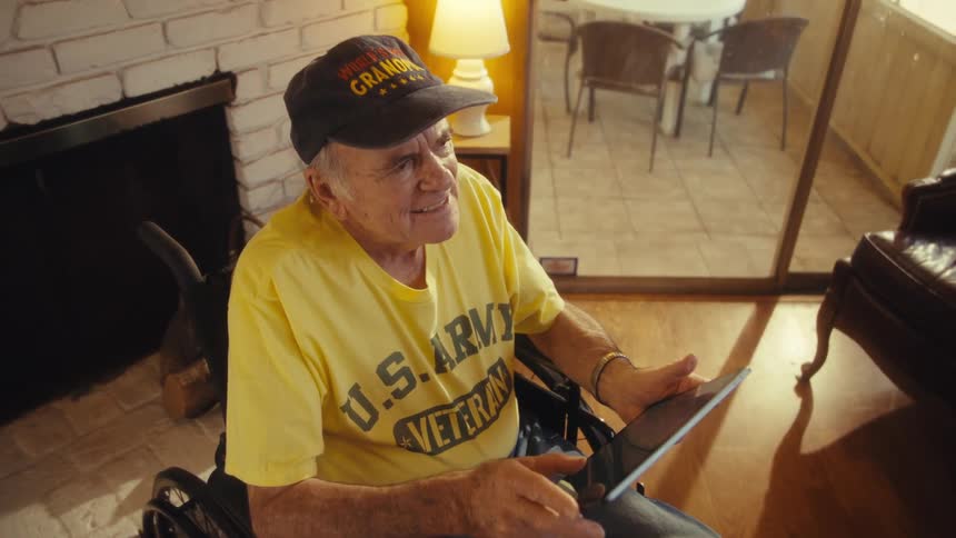 Veteran in a wheelchair smiles while holding a tablet in the living room