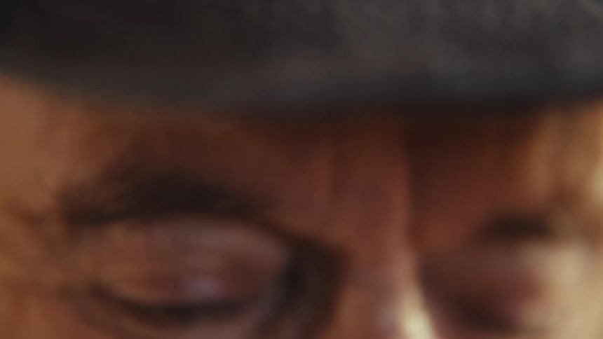 Elderly man wearing a baseball cap that says worlds best grandpa while smiling indoors during day time