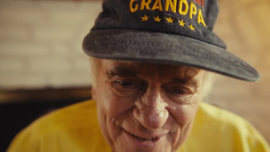 Elderly man in a cap smiles in a closeup lit by natural light