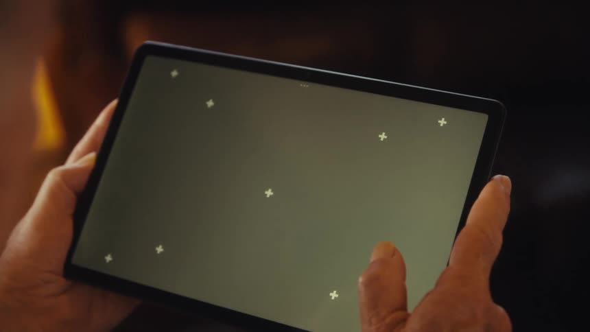 Elderly man sitting at home holds a tablet while viewing it