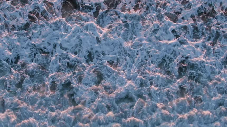 The surface of the ocean moves as waves crash and create white foam