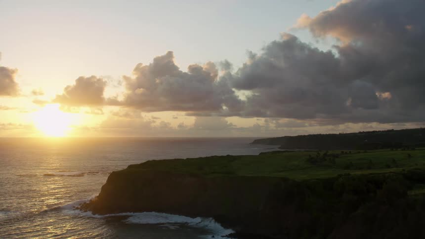 Aerial flyover of a coast lined with rocky cliffs as the sun is low
