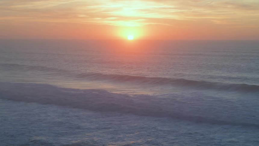 Ocean waves wash upon the shore while the sun is setting