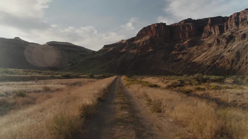 Road path leading toward the mountains with a distant mountain range visible on the horizon