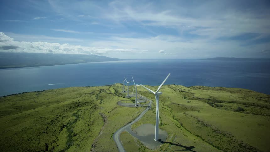 A drone view of a hill with wind turbines in rows and a large body of water in the background