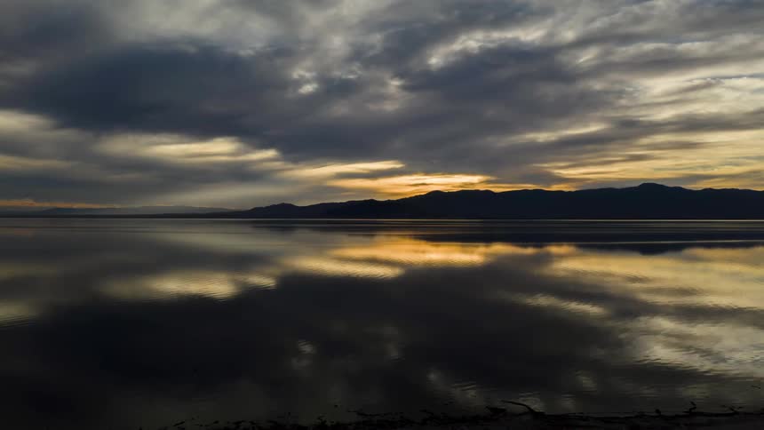 A calm tranquil lake reflects the dramatic clouds and vibrant colors of the setting sun the reflection on the water is so clear that it looks like a perfect mirror image of the sky above