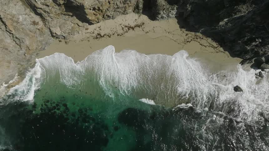 A shot shows a view of ocean waves coming into the shore of a beach surrounded by rocks