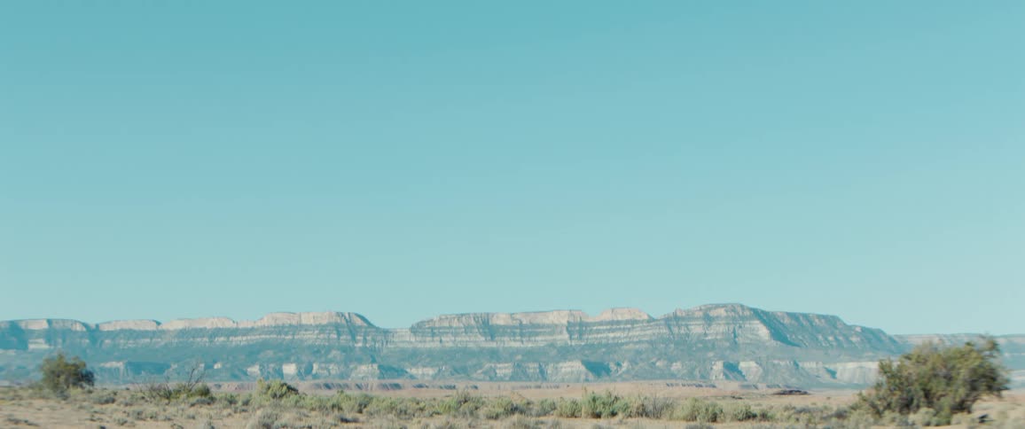 Flat foreground with layered mesa mountains under a clear desert sky