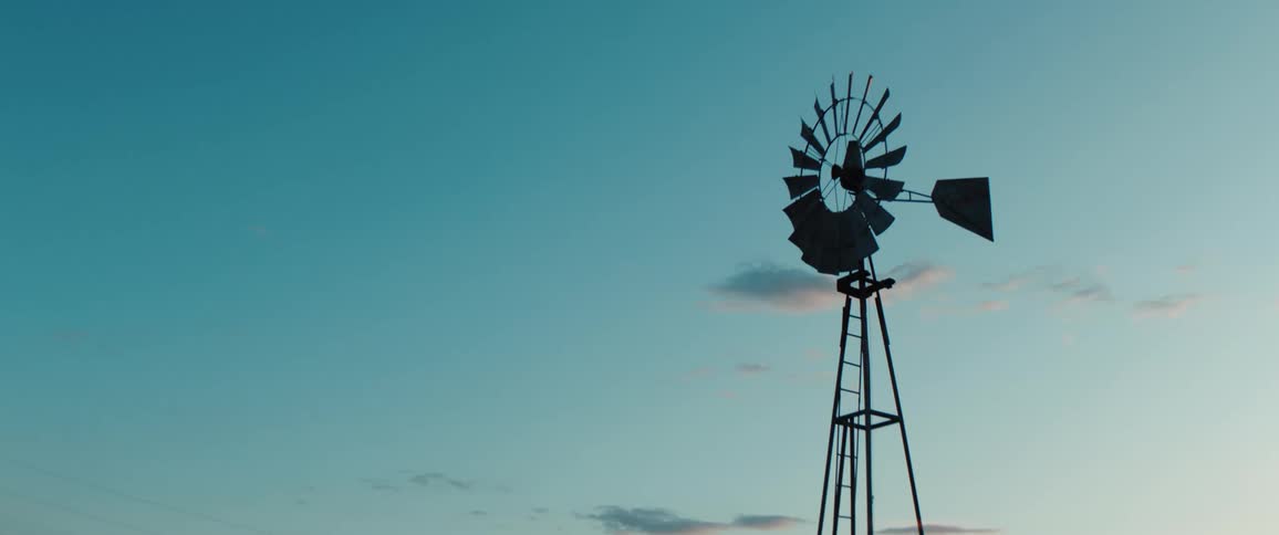 Metal windmill rises against the blue sky at sunset