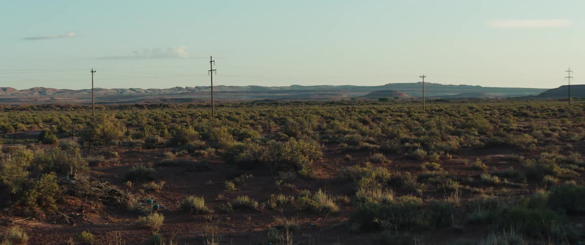 Wide desert landscape with scattered shrubs and power lines under a clear sky