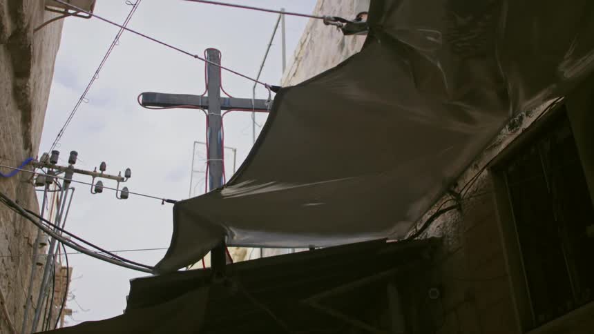 A rope secured tarp is above a door beside a cross