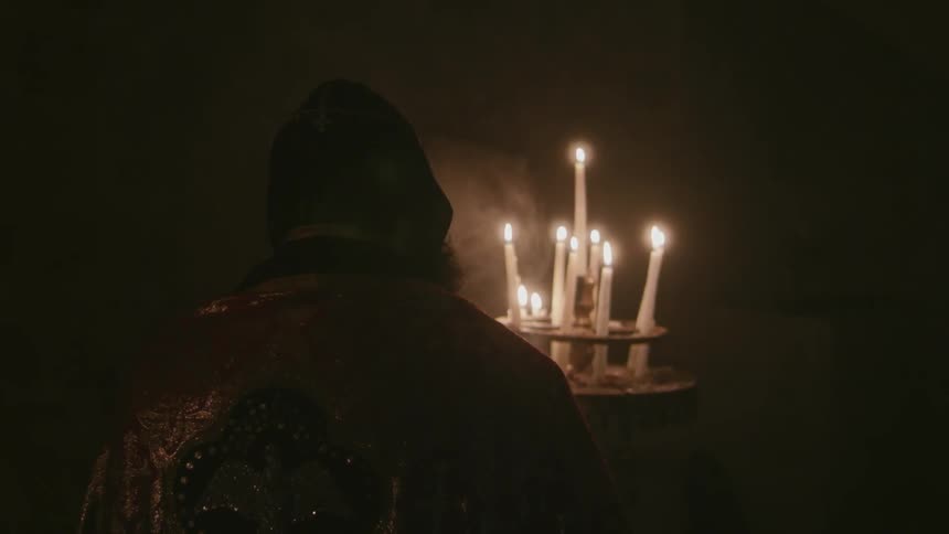Man in an ornate robe kneels before burning candles