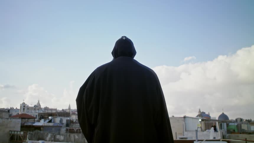 A man in a rote is standing before a town
