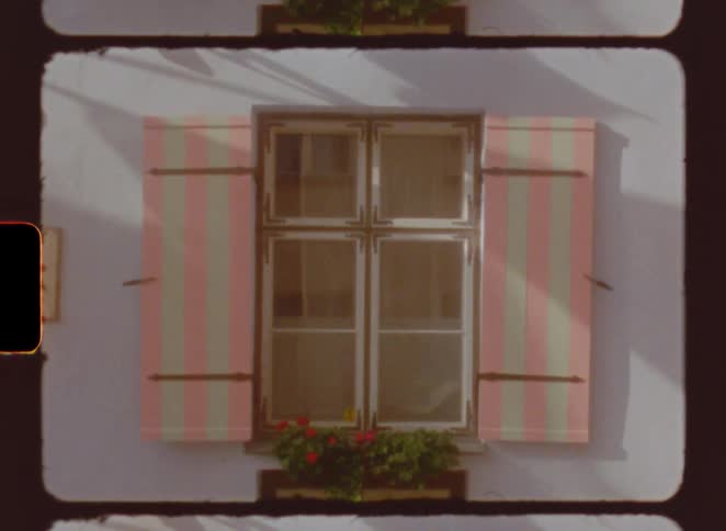 Window with pink and white striped shutters and red flowers at the base