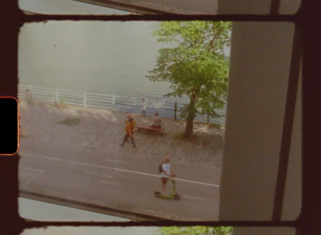 People ride a bicycle and a scooter along a sidewalk at the waters edge