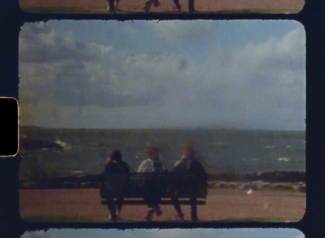 Three people sitting on a bench watch the rough sea