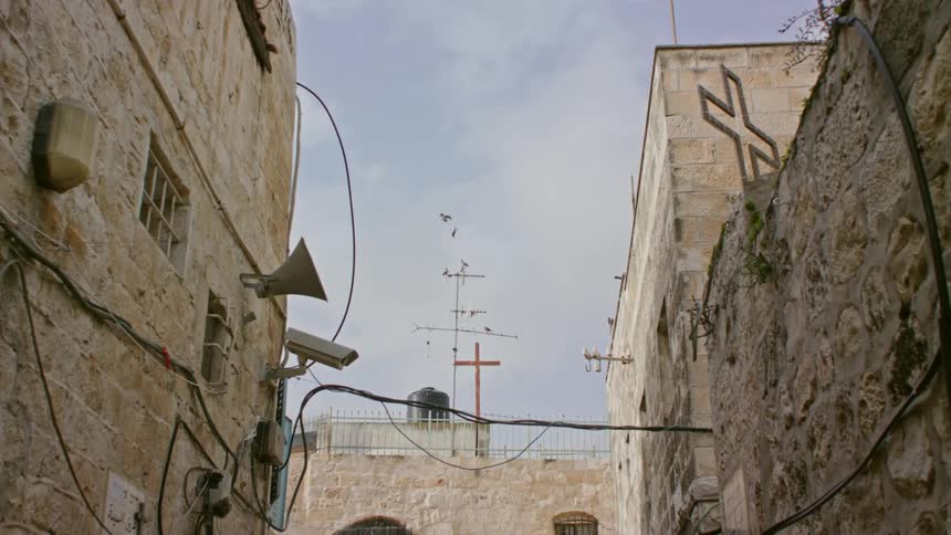 Birds fly over stone building with surveillance camera and megaphone