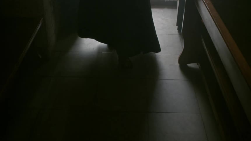 A robed clergyman walks into a dark room