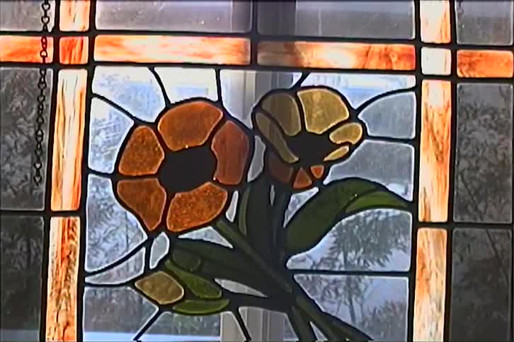 A window with an artistic design showing snow and trees outside through the glass