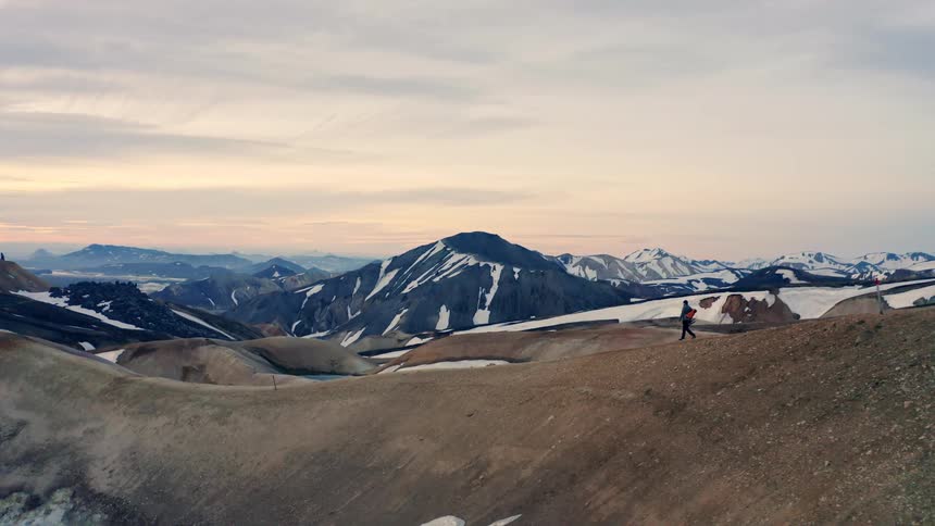 A person hiking on a hill with a mountain range in the background partially covered in snow in the wilderness at midday
