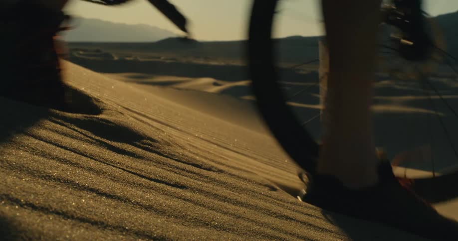 The person pushes their bike over the sand dune