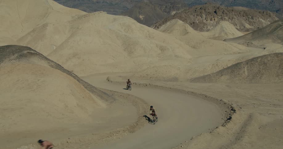 Cyclists riding on a winding road between rocky formations in the desert