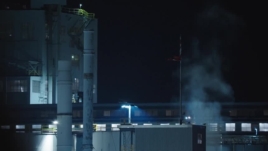 Steam is coming out of a vent on top of an industrial building at night