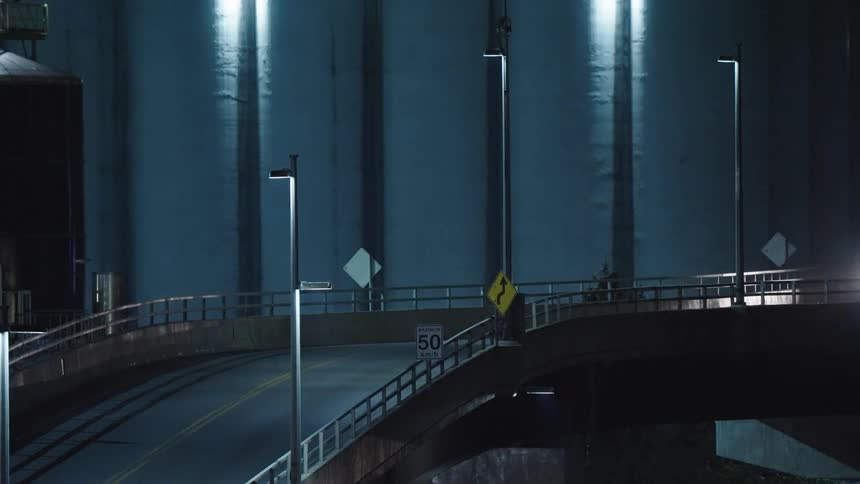 A flatbed semi truck drives on a road next to a bunch of silos